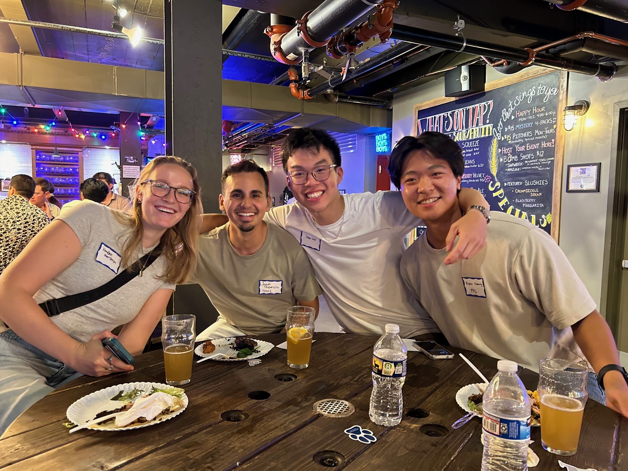 A group of four young professionals gathering behind a table at a social event with food and drinks smiling