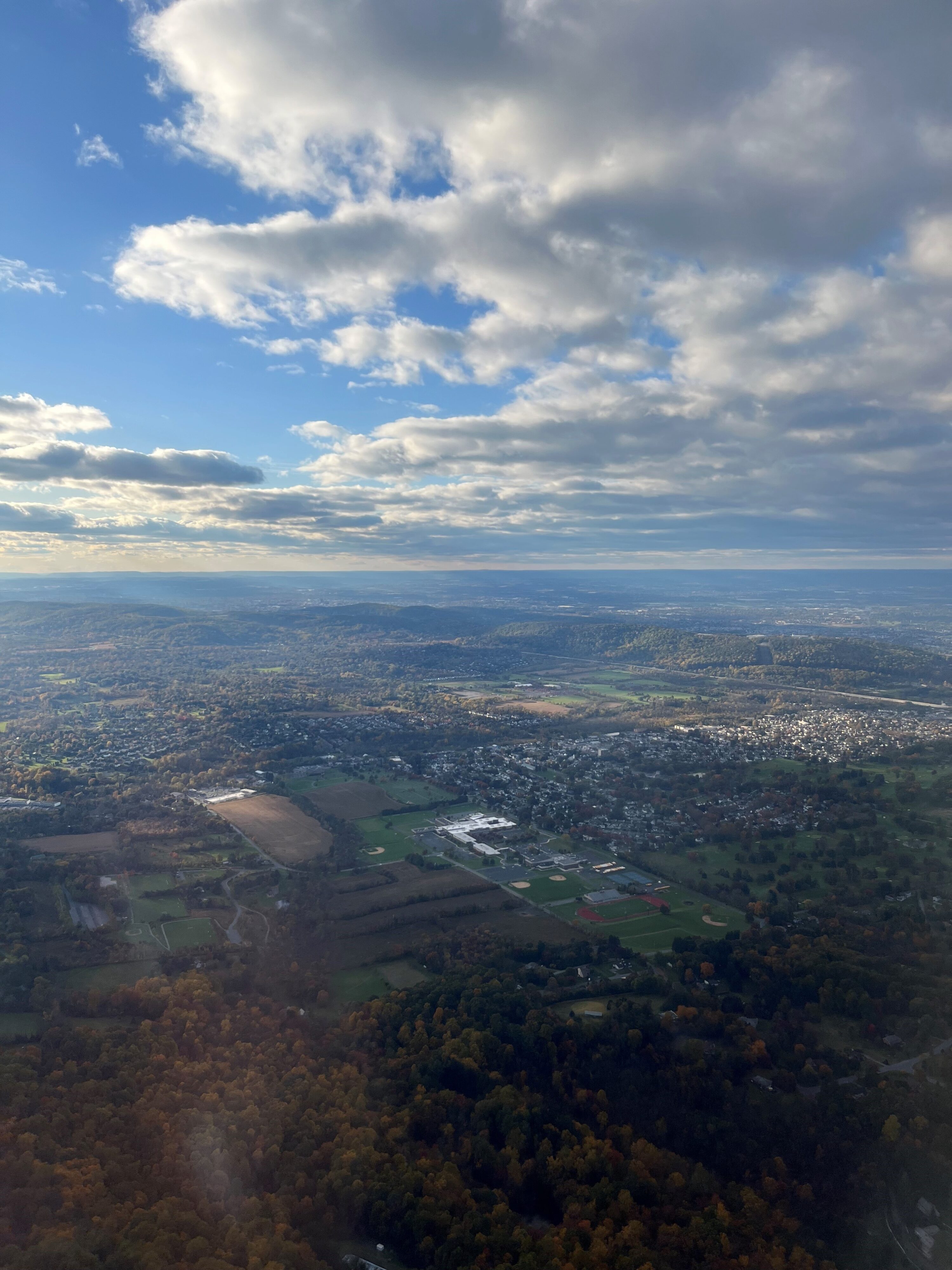 Image from airplane overlooking the Lehigh Valley with clouds in skies and a mix of rural areas and developed cities below. Reflecting